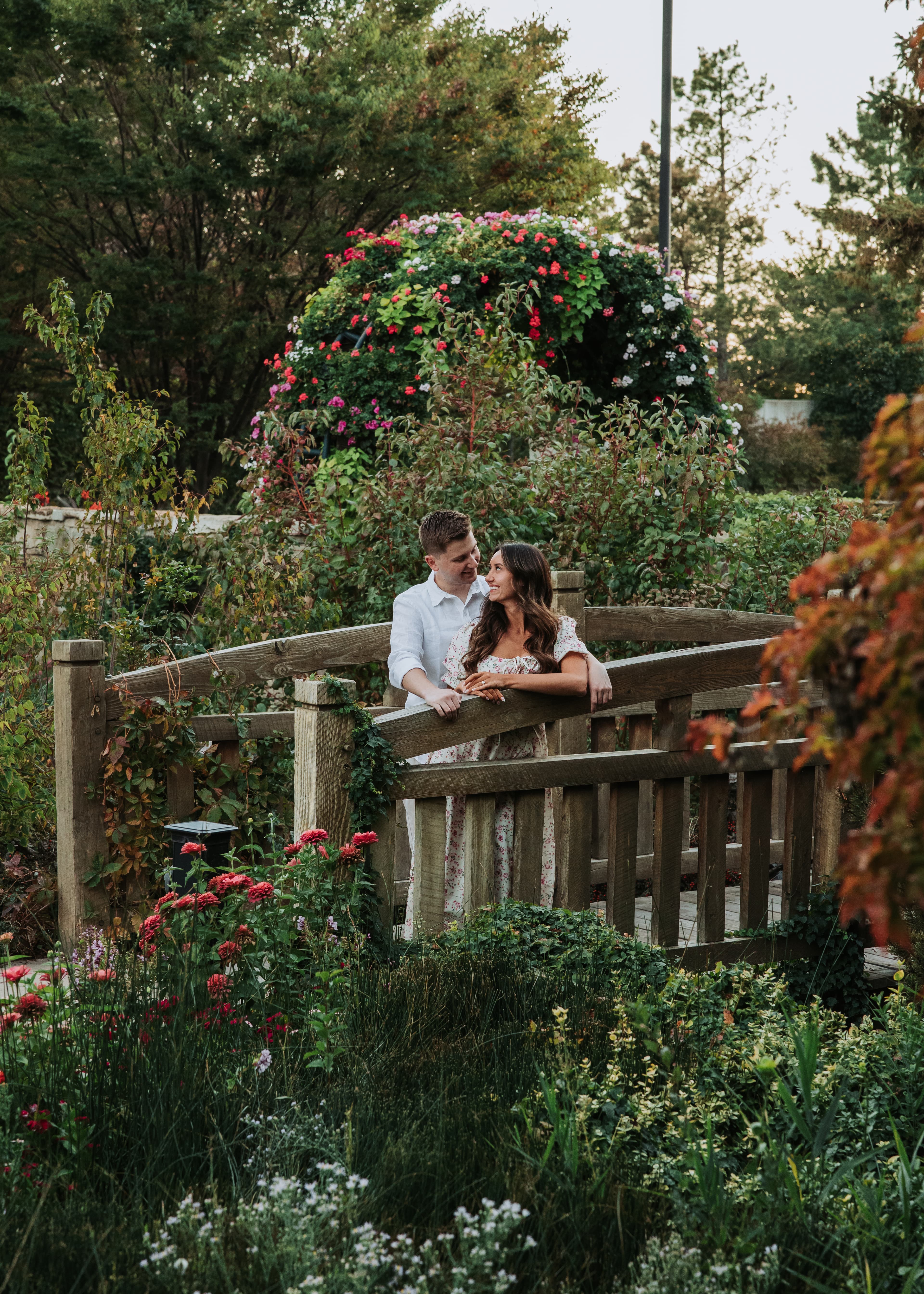 Bre and Bronson on a wooden bridge surrounded by flowers and greenery